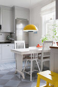 Weißer Holztisch mit Stühlen, darüber Hängelampe in Wohnküche