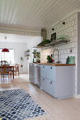 Grey kitchen counter against tiled wall, blue-and-white rug on pale wooden floor and dining room in background