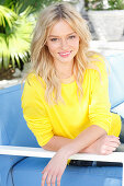 Junge, blonde Frau in gelbem Pulli auf Polsterbank sitzend im Freien