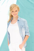 A young blonde woman wearing a white top and a denim shirt against a blue background