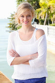 A young blonde woman wearing a white top and a jumper by the sea