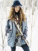 Junge Frau mit Hut in grauem Mantel im Schnee