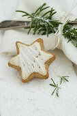 A cinnamon star next to a napkin with a silver fork and a sprig of rosemary