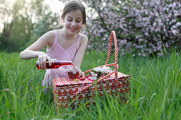 Mädchen giesst Saft in Glas beim Picknick auf Wiese unter Apfelbäumen