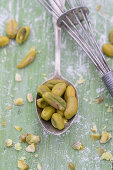 Pistachios on a silver spoon, and an old whisk on a green wooden surface
