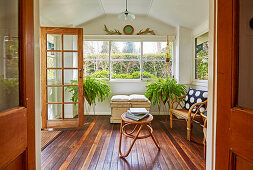 Rattan furniture, a chest and green plants in the winter garden with a rustic wooden floor