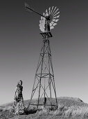 A young woman wearing a long summer dress standing next to a wind turbine (black-and-white shot)