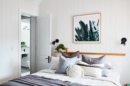 Doppelbett mit Dekokissen und Ablage im Schlafzimmer mit weißer Holzverkleidung