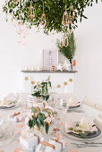 Modern place settings on white Christmas table below bunch of mistletoe