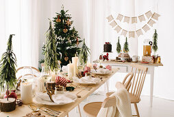 Table festively set with white pillar candles and small Christmas trees