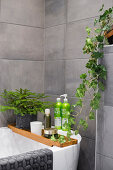 Badewanne mit Weihnachtsdekoration und Grünpflanze im Badezimmer mit grauen Wandfliesen