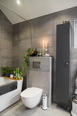 Bathtub and toilet in bathroom with grey wall tiles