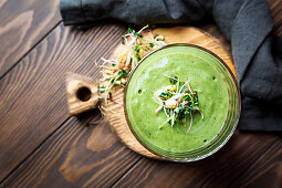 Green vegan smoothie with spinach, banana and sprouted seeds on dark wooden background