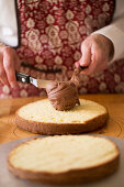 A cake being made: chocolate cream being spread onto a halved cake