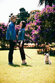 A young couple wearing matching outfits (denim jackets and black trousers) in a park with a dog