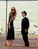 A brunette woman wearing and a pilot at an airport separated by a fence