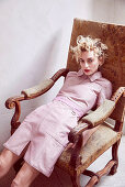 A blonde woman wearing a pink dress slouching on an antique chair