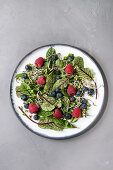 Green vegan salad with berries strawberry, blueberry, sprouts, young beetroot leaves on ceramic plate