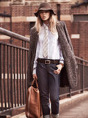 A young woman wearing a hat, a white shirt, a tie, jeans and a coat