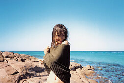 Junge Frau in schulterfreiem Pulli am Strand
