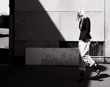 A young woman wearing a black blazer and rolled-up jeans in front of an industrial building (black-and-white shot)