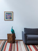 Sculpture of peacock next to grey sofa on striped rug