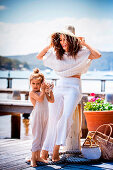 A dark-haired woman wearing a white outfit on a jetty with a little girl