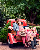 A young couple sitting on the bed of a pick-up truck with Christmas presents