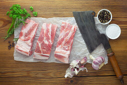 Raw pork ribs with a cleaver and various ingredients on a wooden surface