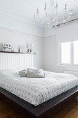Double bed with wooden headboard and white chandelier in bedroom
