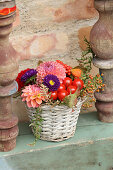 Colourful arrangement of autumn flowers and tomatoes in basket
