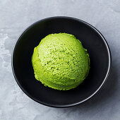 Green tea matcha ice cream scoop in black bowl on a grey stone background