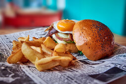 A hamburger with a fried egg and french fries on newspaper