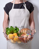 A woman holding a wire basket with bread, vegetables, apricots and other foods