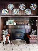 Fireplace and built-in benches in niche with wooden cladding, colorful wall plates above