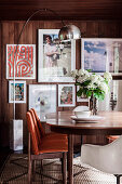 Tisch mit Stühlen und Bogenlampe im Esszimmer, Bilder an holzverkleideter Wand
