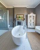 Sofa, oval bathtub and open fireplace in comfortable bathroom