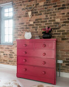 Old chest of drawers painted hot pink against brick wall