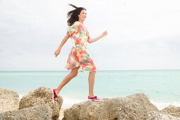 A brunette woman wearing a colourful dress jogging along a beach
