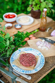 Raw burgers and ingredients on a table outside
