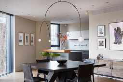 Designerlampe über Esstisch mit Stühlen in offenem Wohnraum, im Hintergrund Einbauküche