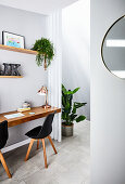 Schwebender Schreibtisch mit schwarzen Stühlen, neben Durchgang mit Zimmerpflanze