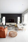 TV against black wall, white designer armchairs, coffee table and brown leather armchair in elegant living room