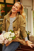 A blonde woman wearing a striped top, a jacket and jeans holding a bunch of flowers