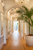 Elegant hallway with round arches and chandeliers, in the foreground a palm tree