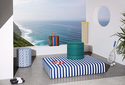Matratze und Sitzpouf mit bunten Bezügen auf Terrasse mit Meerblick