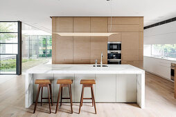 Designer kitchen with a central block made of marble and bar stools in an open living room with a glass front