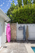 Pink surfboard on natural stone wall, next to white painted wooden fence