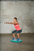 A young woman performing a knee bend with weights on an unstable surface