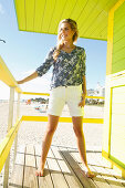 A blonde woman wearing shorts and a floral tunic outside a beach house